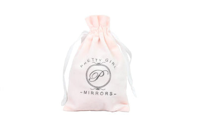 A blush pink soft drawstring bag with white ribbon handles.